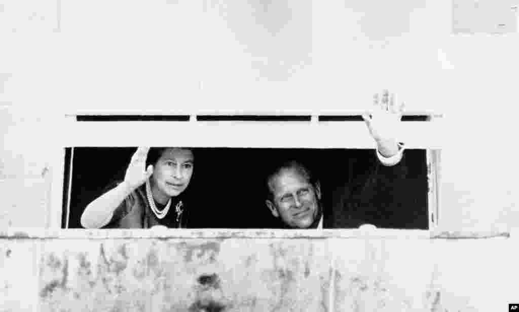 Nữ hoàng Elizabeth II và phu quân, Hoàng tế Philip, vẫy chào đám đông, ngày 10 tháng 8 năm 1977, từ một cửa sổ khép hờ trong Lâu đài Hillsborough, cách Belfast, Bắc Ireland 12 dặm về phía nam. Bạo lực xảy ra trong chuyến thăm nhân dịp đại lễ bạc của Nữ hoàng tới tỉnh này. 