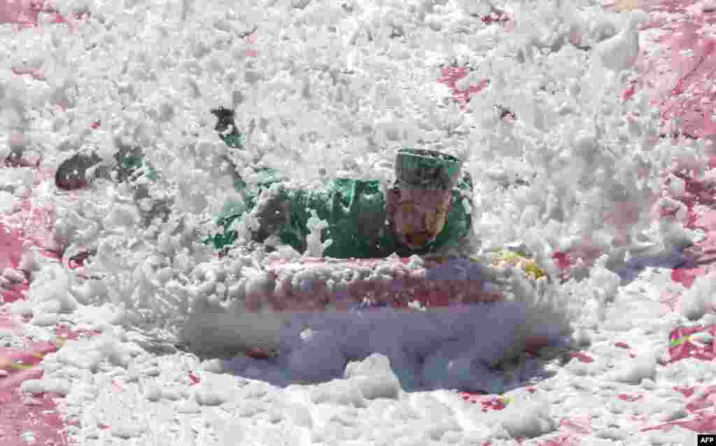 A participant moves down a water slide during the Saltibarsciai Slip and Slide competition during the Pink Soup Fest in Vilnius, Lithuania, June 10, 2023.