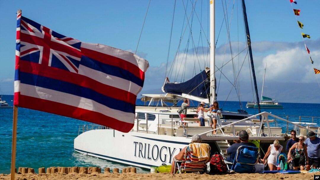 FILE - Tourists get off of a Trilogy Excursions boat arriving on Kaanapali Beach in front of a flag of Hawaii planted in the sand, Dec. 6, 2023, in Lahaina, Hawaii.