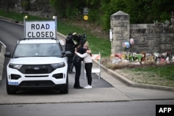 Seorang perempuan memeluk seorang polisi di pintu masuk kampus Kovenan di Gereja Presbiterian Kovenan, Nashville, Tennessee, 28 Maret 2023. (Foto: Brendan SMIALOWSKI/AFP)