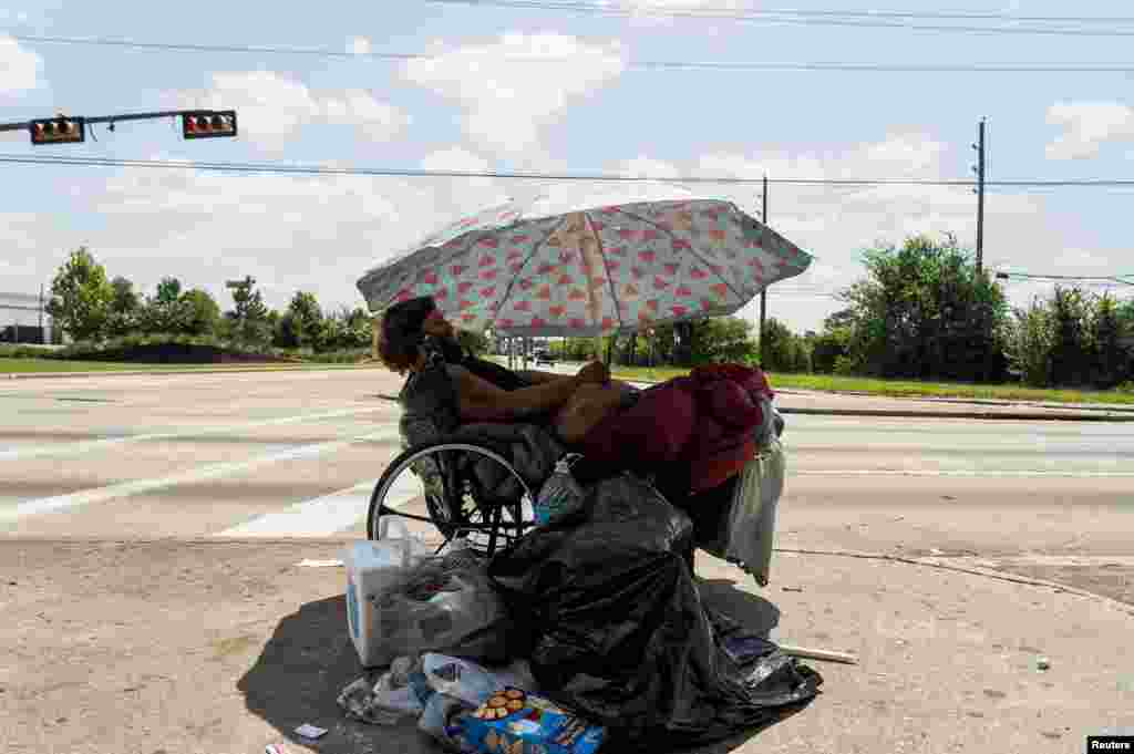 Tony, a homeless man, sits under his umbrella to avoid sun light during hot weather in Houston, Texas, June 28, 2023.