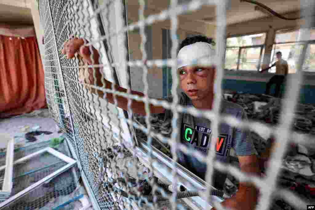 An injured boy stands by a window lattice in a destroyed classroom where people were sheltering at a school run by the U.N. Relief and Works Agency for Palestine Refugees (UNRWA) that was previously hit by Israeli bombardment, in the Nuseirat camp in the central Gaza Strip.