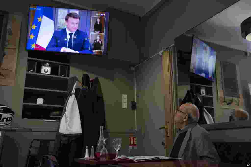 A man at a cafe watches French President Emmanuel Macron speaking during a television interview with journalists, in Marseille, France.
