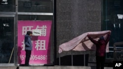 北京街頭一名女子在一家空置招租店鋪外曬棉被。（2023年12月17日）