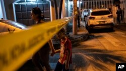 Los residentes pasan junto a la cinta policial que marca la escena del crimen para llegar a su casa en Durán, la ciudad cercana a Guayaquil, Ecuador, después de la medianoche del 28 de septiembre de 2023. 