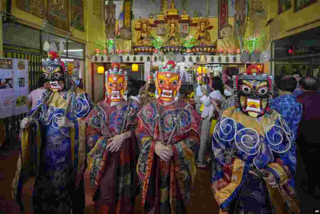 Monks wearing magnificent costumes and masks perform prayers before the Thangka, or traditional painting of Lord Buddha, at a Tibetan temple during Wesak day celebration in Ipoh, Malaysia.