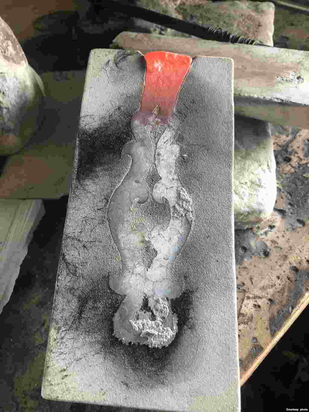 The artist ties the carved block to a flat, uncarved block (not shown), pouring molten silver through the channel at the top.