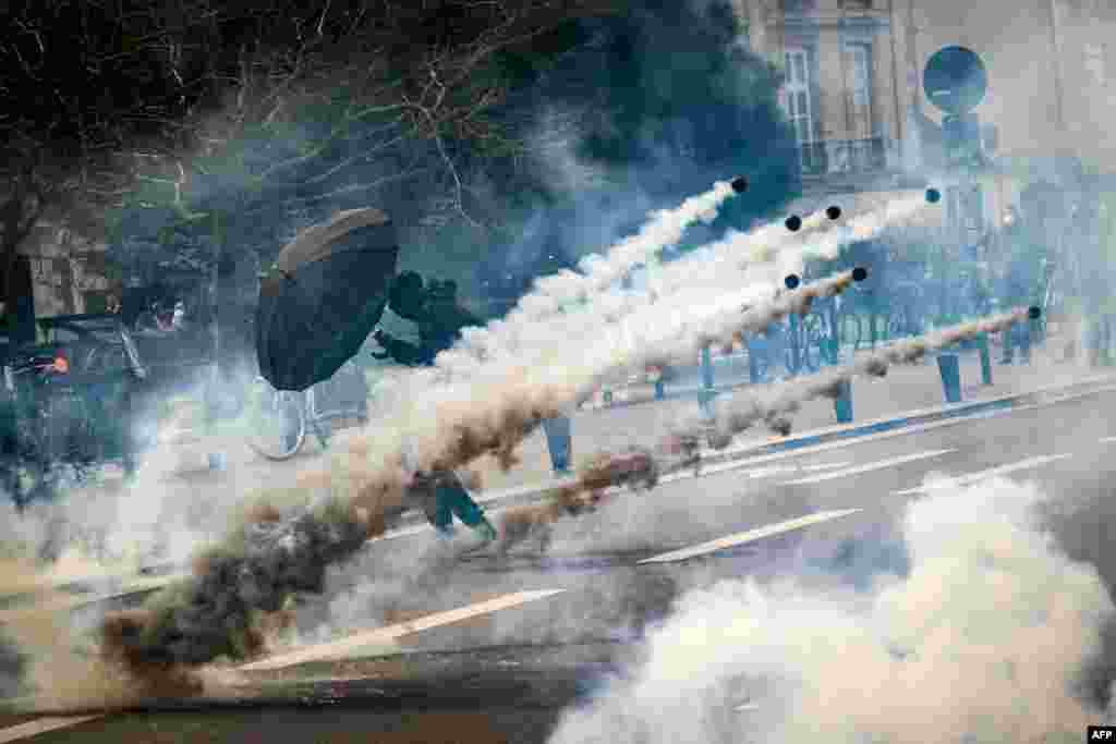 A protester holds an umbrella amid tear gas fired by security personnel during the 8th day of strikes and protests across the country over the government's proposed pension overhaul, in Nantes, France.