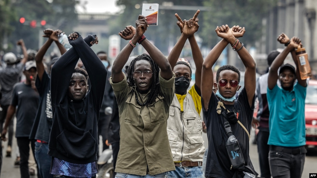 FILE - Protesters make signs with their arms in front of Kenya police officers during a demonstration against tax hikes as Members of the Parliament debate the Finance Bill 2024 in downtown Nairobi, June 18, 2024. 