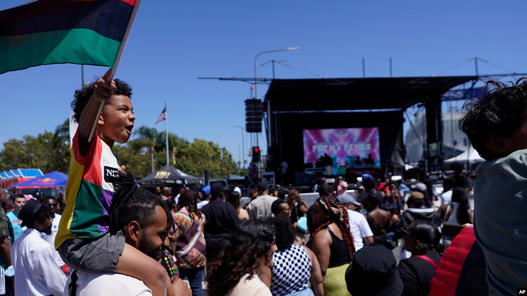 FILE: Julien James carries his son, Maison, 4, holding a Pan-African flag, to celebrate during a Juneteenth commemoration in Los Angeles on June 18, 2022.