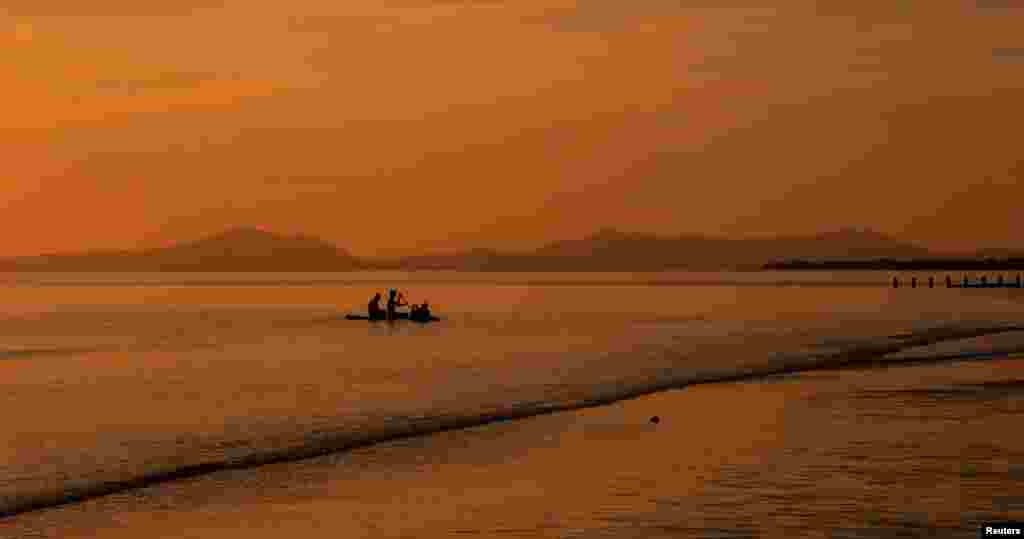 Children play on a paddleboard as the sun sets over the beach in Barmouth, Britain, May 29, 2023.