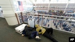 Dua orang pelancong tidur di bandara sementara para pelancong lainnya antre melewati pos pemeriksaan keamanan di Bandara Internasional Denver saat badai musim dingin melanda AS, 23 Desember 2022.
