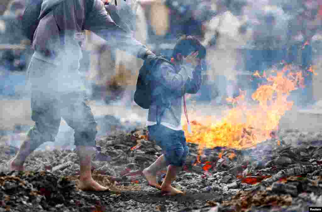 A boy and a man walk next to flames as they walk over coal with barefoot at the fire-walking festival, called Hiwatari Matsuri in Japanese, at Mt.Takao in Tokyo, Japan, March 13, 2022.