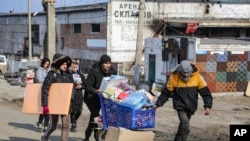 FILE -Wakazi wakiwa wamebeba maji kutoka katika ghala la chakula, katika eneo ambalo linadhibitiwa na serikali ya Jamhuri ya Watu wa Donetsk, nje ya mji wa Mariupol, Ukraine, Ijumaa, March 18, 2022. (AP Photo/Alexei Alexandrov)