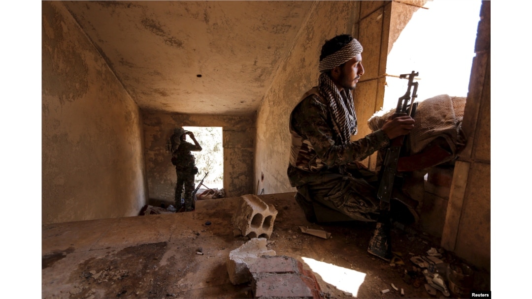 FILE - Kurdish People's Protection Units (YPG) fighters take up positions inside a damaged building in al-Vilat al-Homor neighborhood in Hasaka city, Syria.