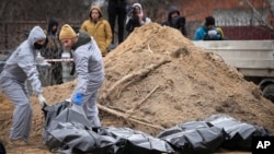 Men wearing protective gear exhume bodies of some of the civilians killed during the Russian occupation of Bucha, on the outskirts of Kyiv, Ukraine, April 13, 2022.