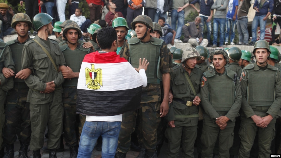 An anti-Mursi protester with an Egyptian flag around his shoulders talks to soldiers standing guard outside the Egyptian presidential palace in Cairo December 9, 2012.