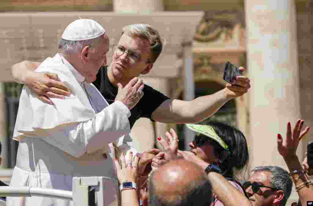 A man hugs Pope Francis to take a selfie after he had climbed on the popemobile at the end of the weekly general audience in St. Peter's Square at the Vatican.