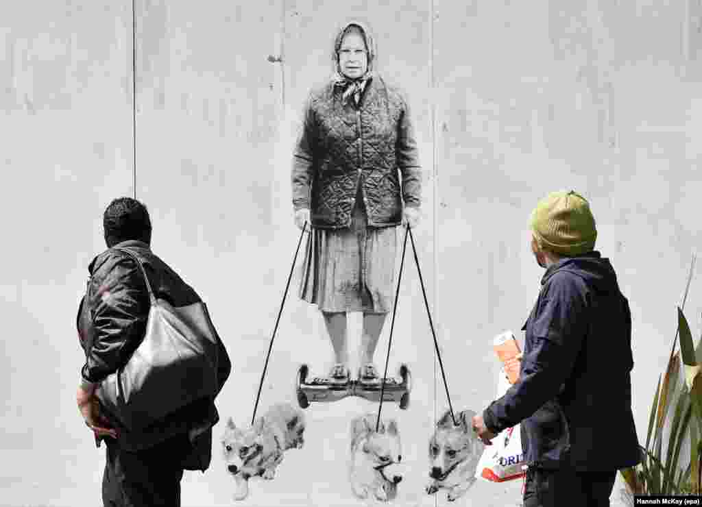 Pedestrians look at a new mural depicting Britain's Queen Elizabeth II that is spray-painted onto the external wall of a house in south-east London.