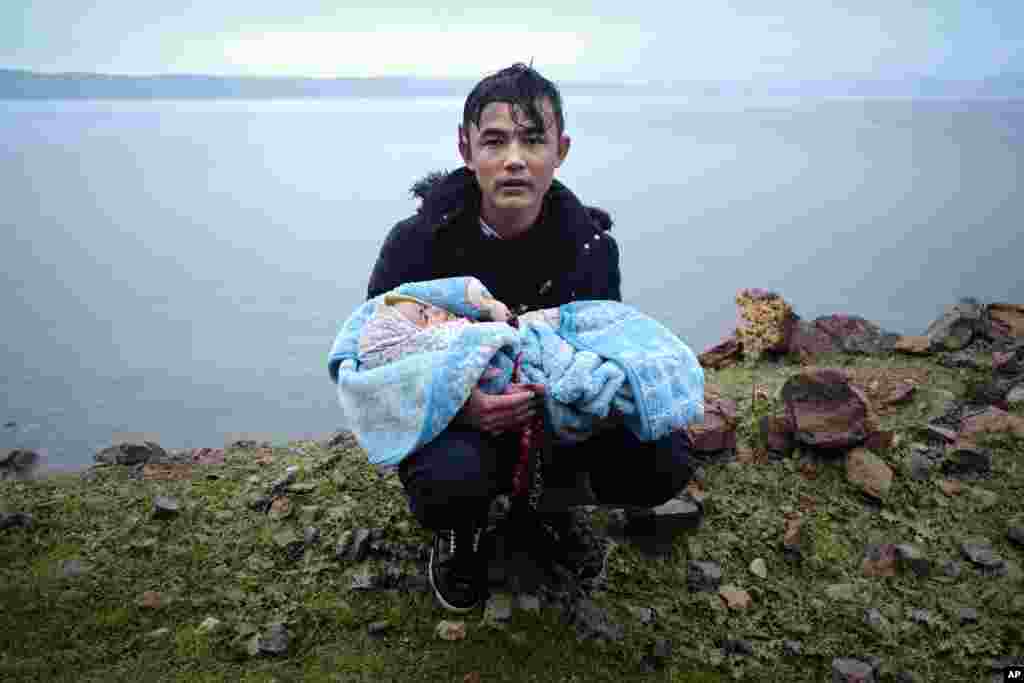 A migrant holding a baby pauses on the side of the road while walking to the village of Skala Sikaminias, on the Greek island of Lesbos, after crossing on a dinghy the Aegean sea from Turkey.