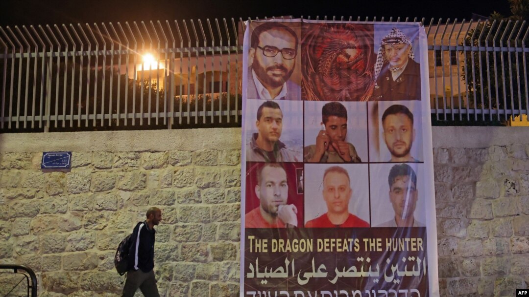 FILE - A man walks by a banner depicting the six Palestinian prison escapees, in the West Bank town of Bethlehem, September 8, 2021.