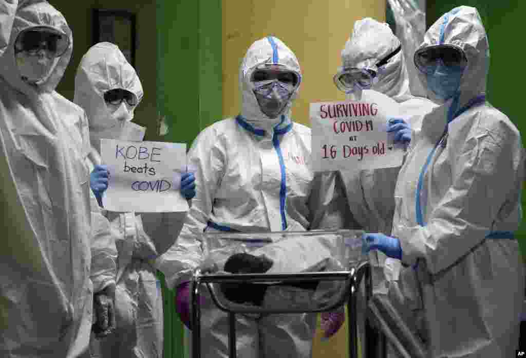 Health workers wearing protective suits holds signs with a 16-day-old baby who recovered from COVID-19 as he is discharged from the National Children's Hospital in Quezon city, Metro Manila, Philippines .