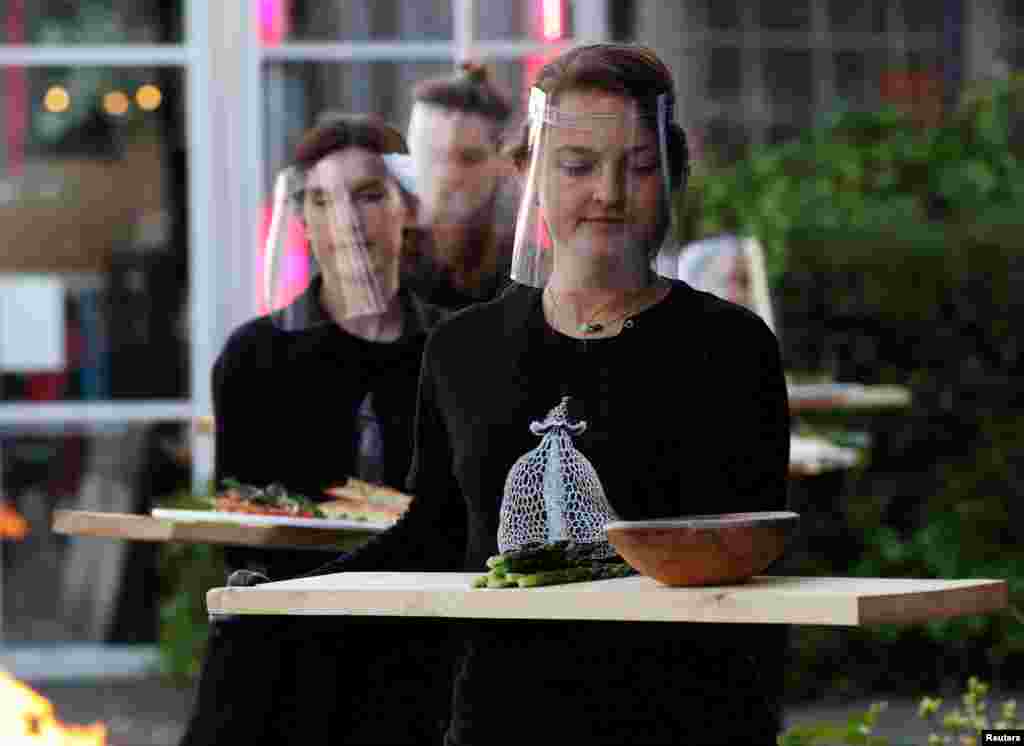 Servers in protective gear carry food at a restaurant which is testing servers providing drinks and food to models pretending to be clients in a safe "quarantine greenhouses" in Amsterdam, Netherlands, May 5, 2020.