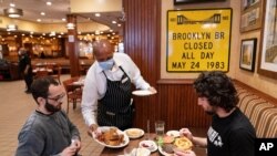 FILE - A waiter serves lunch to clients at Junior's Restaurant in New York. NYC will soon require proof of COVID-19 vaccinations for anyone who wants to dine inside at a restaurant.