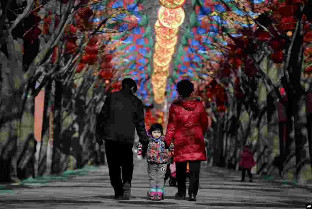 An elderly Chinese couple holds a child standing on a scooter as they walk under colorful decorations for a temple fair ahead of the Chinese Lunar New Year at Ditan Park in Beijing, Feb. 2, 2016. Chinese will celebrate the Lunar New Year on Feb. 8
