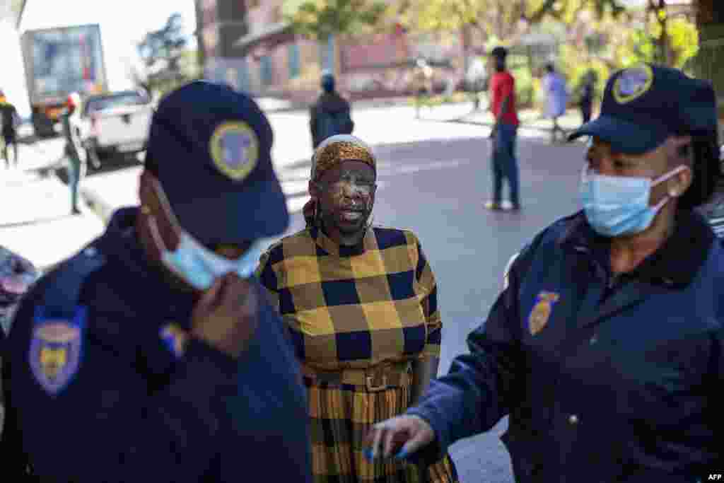 A woman reacts in pain after being pepper sprayed by a member of the South African Police Service, not visible, for not wearing a face covering, as members of the Johannesburg Metro Police Department walk away, in Hillbrow, Johannesburg.