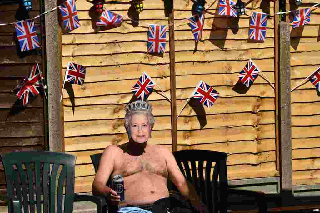 Terry Livesey, wearing a mask of Britain's Queen Elizabeth II, sunbathes in his garden surrounded by Union flags as people mark the 75th anniversary of Victory in Europe Day, the end of the Second World War in Europe in Portslade, southern England.
