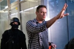 FILE - Russian opposition leader Alexei Navalny gestures as a security officer guards an entrance of his Anti-Corruption Foundation during a raid of its offices, in Moscow, Russia, Dec. 26, 2019.