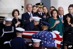 El expresidente George W. Bush, su esposa Laura Bush (izquierda), y otros miembros de la familia observan como el ataúd del ex presidente George H.W. Bush, cubierto por la bandera, es transportado por una guardia de honor militar de servicios conjuntos para permanecer en capilla ardiente en la Rotonda del Capitolio de EE.UU., el 3 de diciembre de 2018.