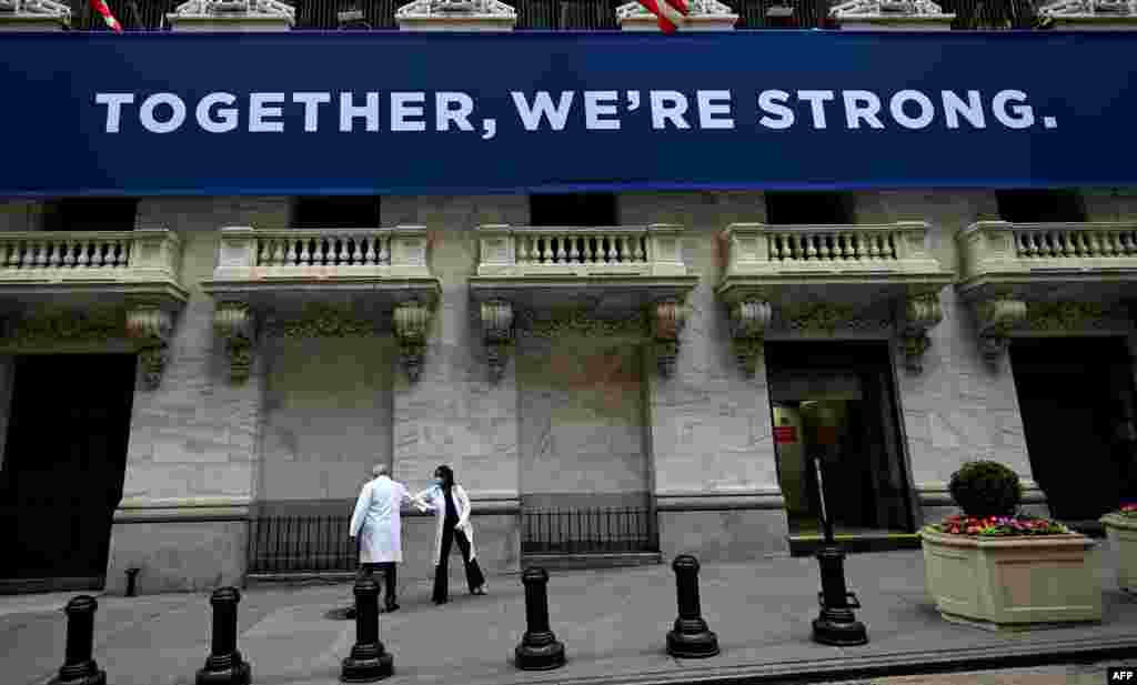 Medical workers bump elbows in greeting as they arrive before the opening bell at the New York Stock Exchange, which opened to in-person activity for the first time in two months, at Wall Street in New York City.