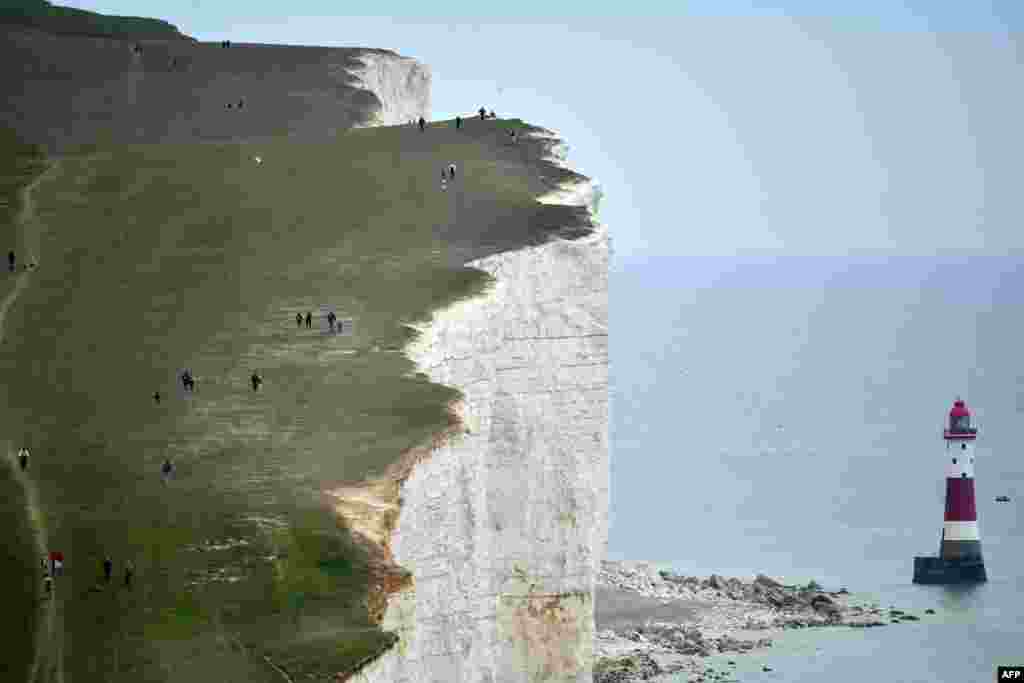 People walk along the cliff-top above the lighthouse at Beachy Head near Eastbourne on the south coast of England following an easing of lockdown rules in England during the COVID-19 pandemic.