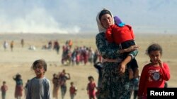FILE - Displaced Yazidis, fleeing violence from forces loyal to the Islamic State group, head toward the Syrian border, Aug. 11, 2014.