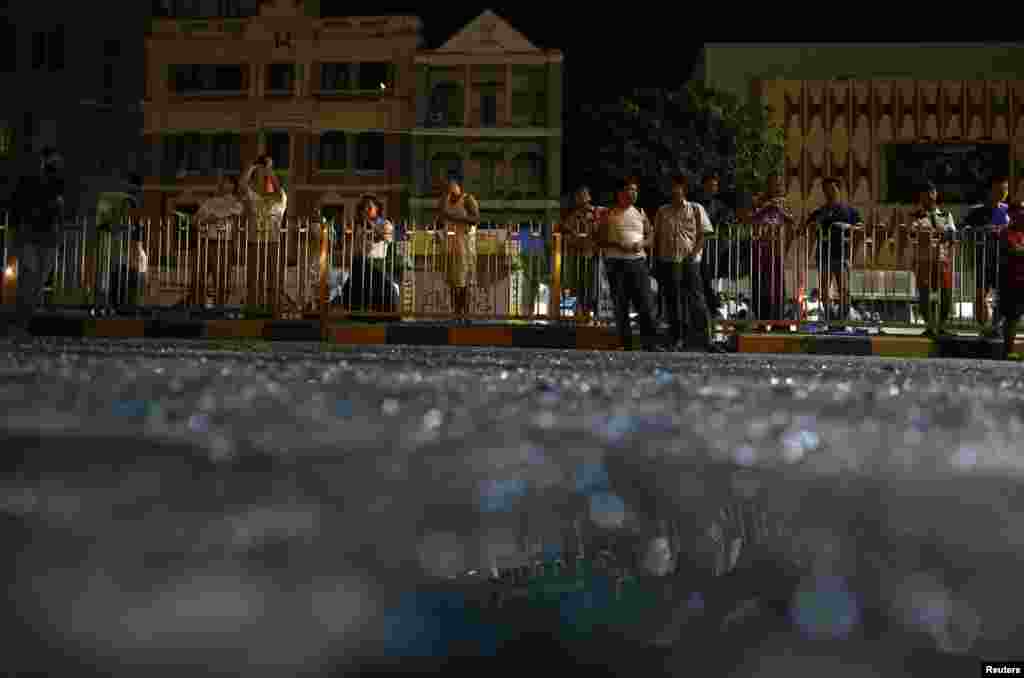 People are reflected in broken glass as they stand in front of Traders Hotel, where an explosion occurred, in central Rangoon, Burma, Oct. 15, 2013.