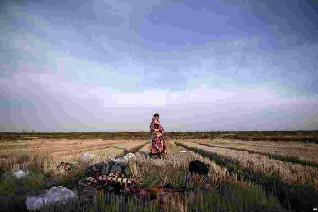 A migrant uses a blanket to warm himself in a field near Edirne, at the Turkish-Greek border.