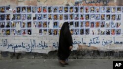 FILE - A Bahraini woman walks past images of political prisoners plastered on a wall in Sanabis, Bahrain, Oct. 22, 2015. Prosecutors in Bahrain said May 15, 2018 that a court has revoked the citizenship of 115 people in a mass terrorism trial.