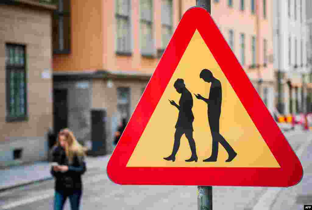 A road sign warns motorists of pedestrians crossing the street while looking at their smartphones near the old town in Stockholm, Feb. 2, 2016.