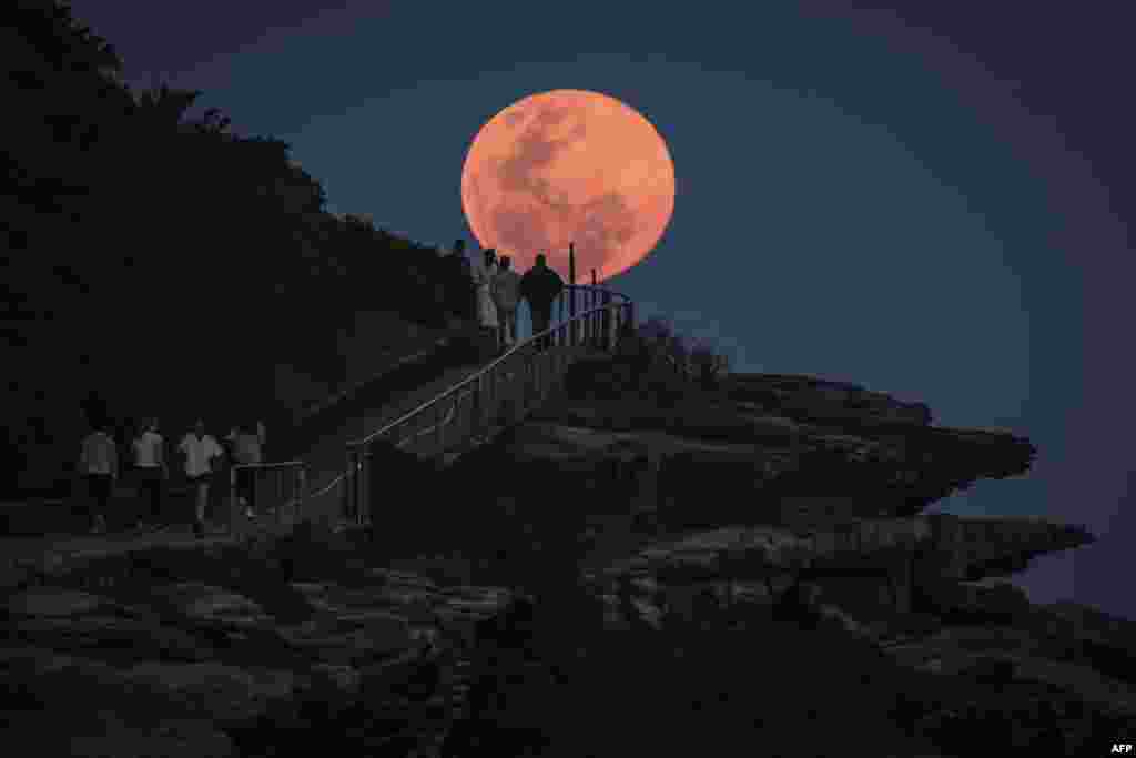A super moon rises behind people standing on a headland near Sydney's Bondi Beach, Australia.