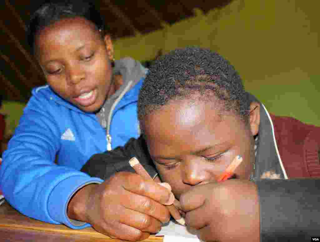 A caregiver helps Sihle to write during a morning school lesson at Ikhaya Loxolo (VOA/ D. Taylor)