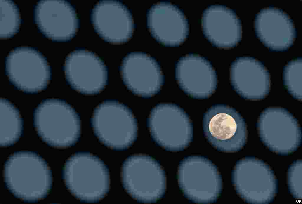 The full moon is seen behind a building's sun shade in Bangkok, Thailand.
