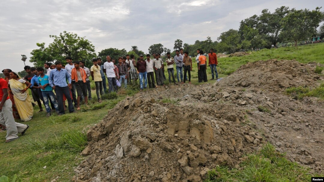 Villagers stand next to mass graves of the school children who died after consuming contaminated meals given to them at a school of the Chapra district, in the eastern Indian state of Bihar, July 18, 2013. 