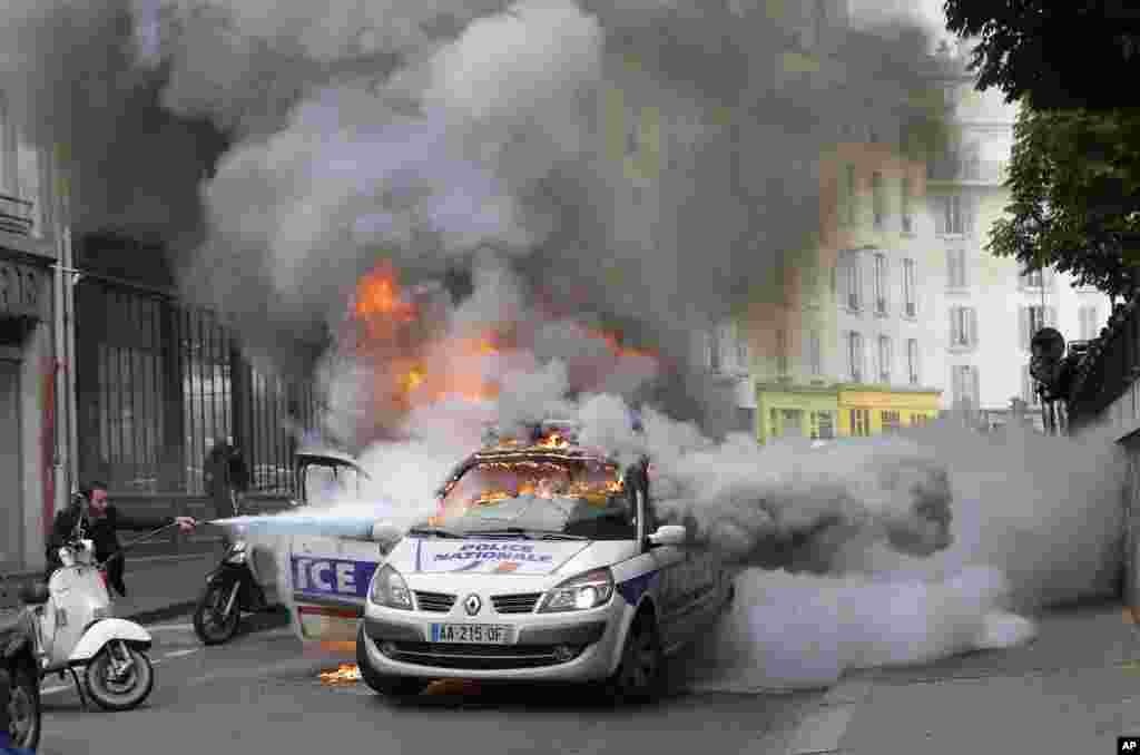 Seorang pria berusaha memadamkan api yang melalap sebuah mobil polisi akibat aksi protes rusuh menentang RUU Perburuhan di Paris, Perancis.
