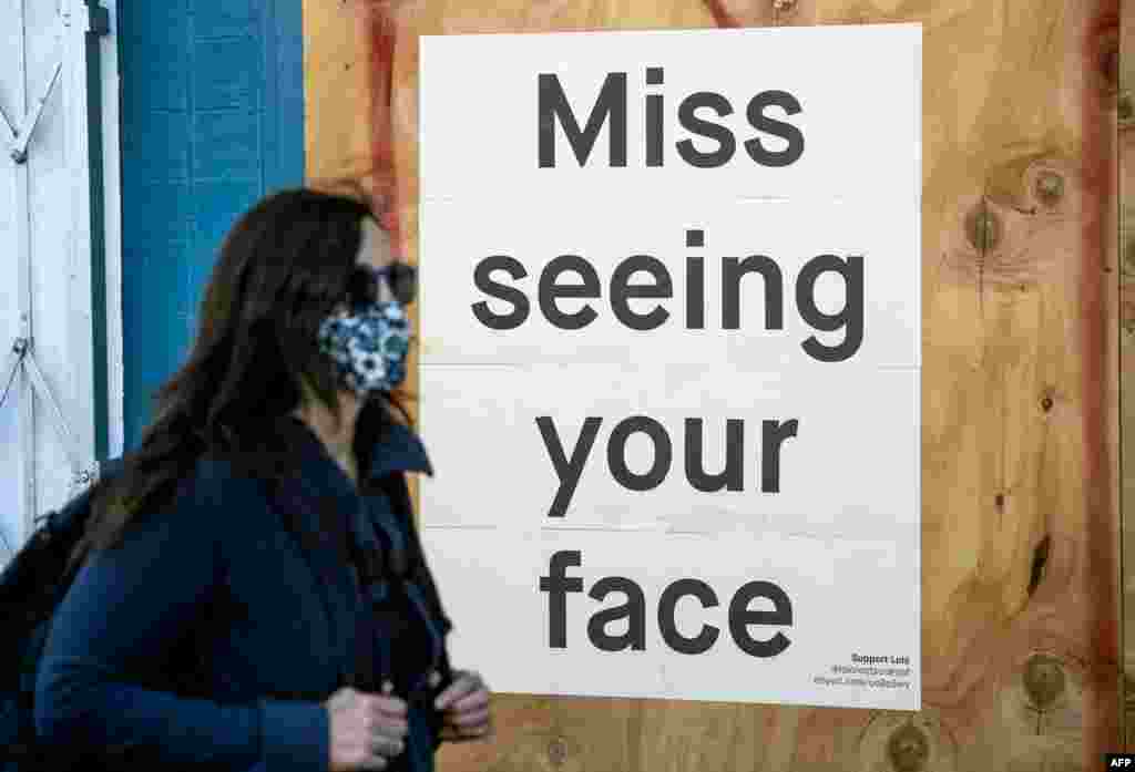 A woman in a face mask walks by a sign posted on a boarded up restaurant in San Francisco, California, April, 1, 2020, during the novel coronavirus outbreak.