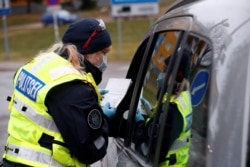 FILE - An Estonian police officer checks documents at the border crossing point as Estonia reintroduces border control and a ban to enter Estonia for foreigners as a preventive measure against the coronavirus in Valga, Estonia, March 17, 2020.