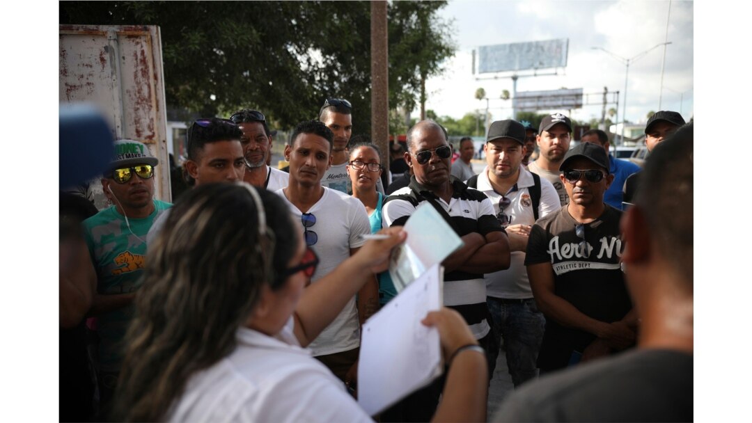 FILE - Migrants listen as a Mexican migration officer verifies their identity on a list Matamoros, Mexico, at the foot of the Puerta Mexico bridge that crosses into Brownsville, Texas, Aug. 2, 2019.