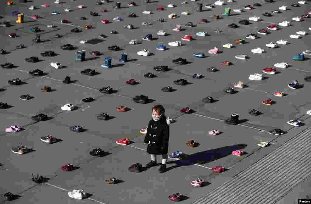 A child wearing a face mask stands surrounded by shoes, after Civil disobedience group Extinction Rebellion laid out 1,500 pairs of children's shoes in Trafalgar Square in central London to demand that government adopts a climate-friendly economic recovery plan.