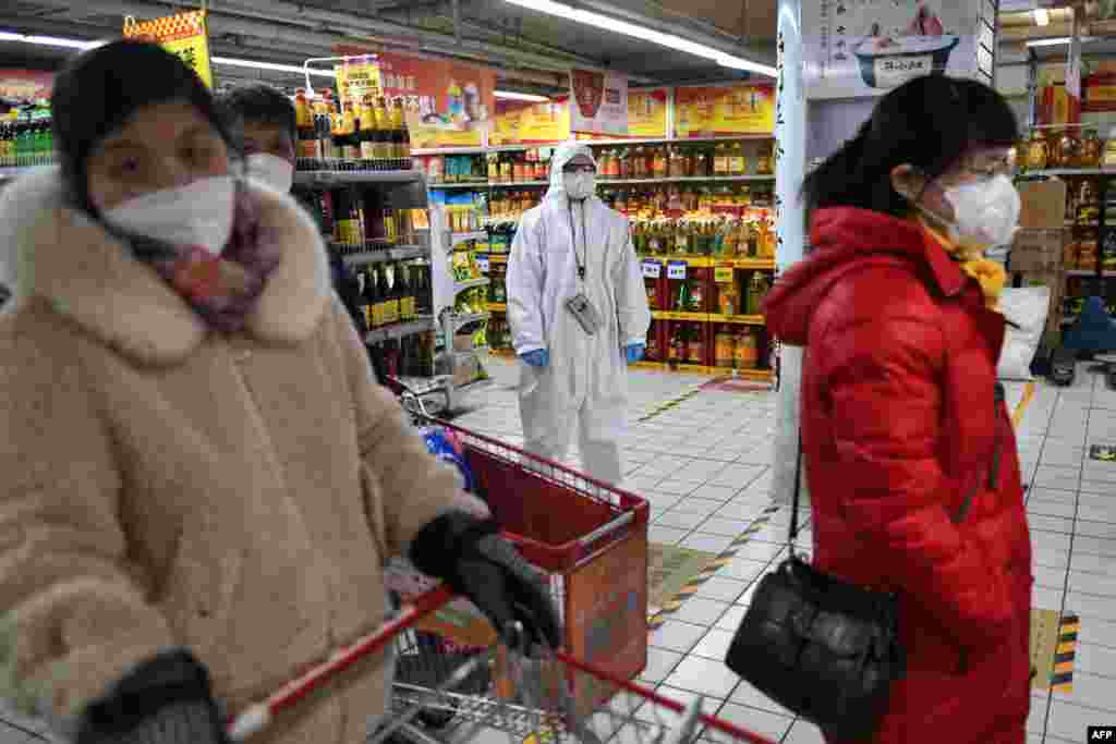 A worker wears protective clothing as a preventive measure against the COVID-19 coronavirus as she watches over customers in a supermarket in Beijing.